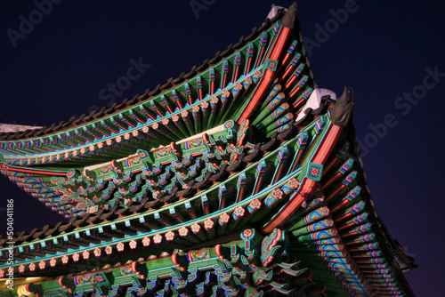 A nighttime shot of the colorful roof structure of a Temple in Seoul, Korea creates a strong contrast to the dark blue night sky. 