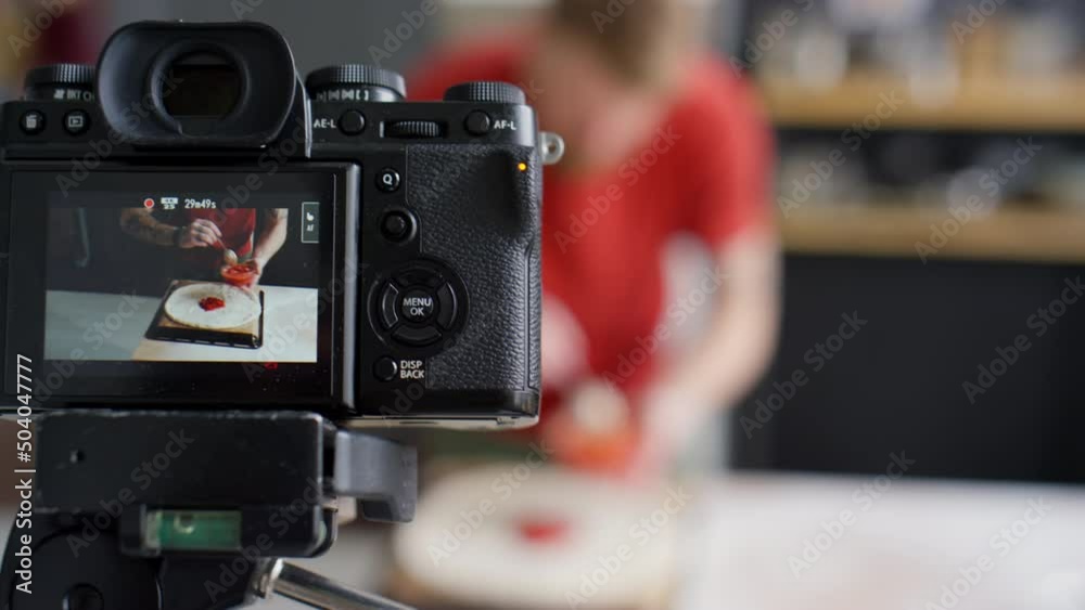 Close up selective focus shot of professional camera filming video of food blogger adding tomato sauce to pizza dough at kitchen table Close up selective focus shot of professional camera filming video of food blogger adding tomato sauce to pizza dough at kitchen table