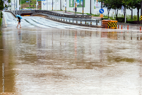 Foto 여름철 집중호우로 침수된 도로, 우산 쓴 젊은 여성-A young woman with an umbrella on a flooded road fr