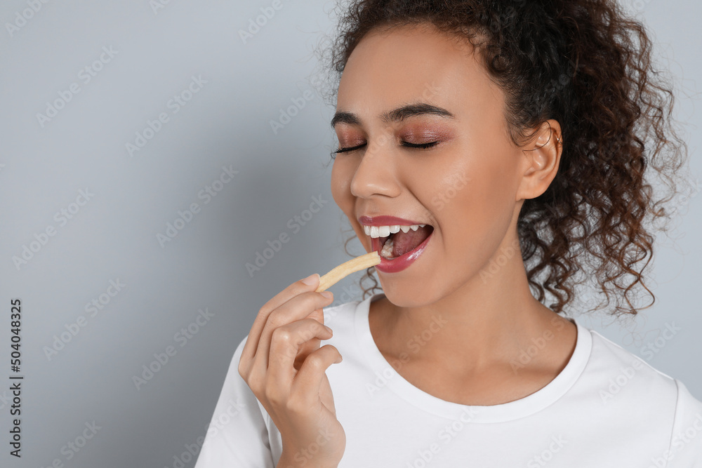 African American woman eating French fries on grey background, space for text African American woman eating French fries on grey background, space for text