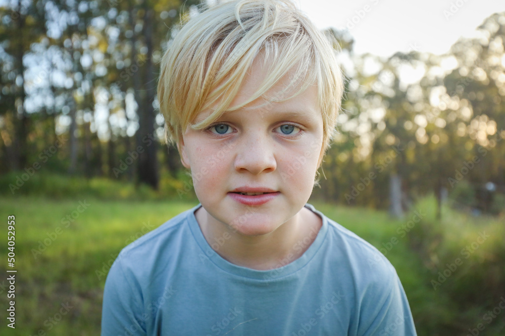 Blonde boy with grumpy expression close up in the bush at sunset Blonde boy with grumpy expression close up in the bush at sunset