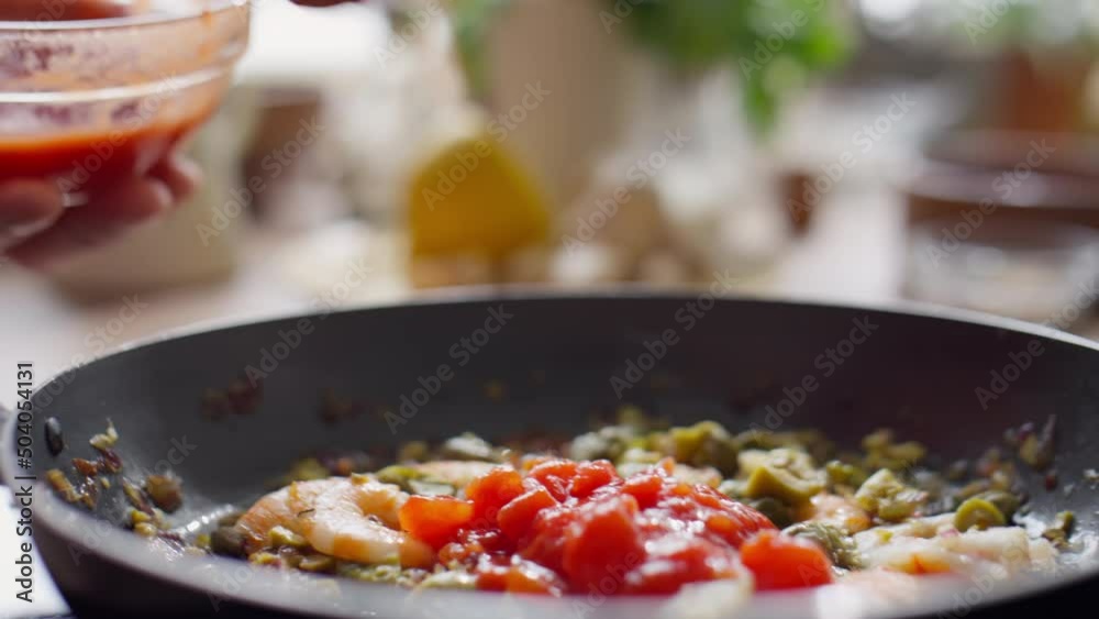 Close up shot of chef hands adding diced tomatoes with spoon to ingredients in frying pan Close up shot of chef hands adding diced tomatoes with spoon to ingredients in frying pan