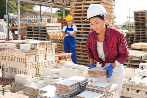 Concentrated asian woman manager working in a building materials store is laying tiles in a warehouse