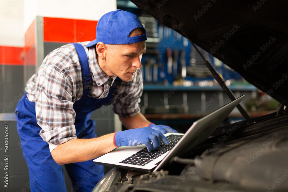Male mechanic using laptop while repairing car in auto service