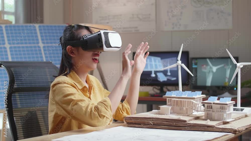 Side View Of Smiling Asian Woman Working With A Model Of Small House Roof Solar Panel Wearing Vr And Showing Touching Gesture
