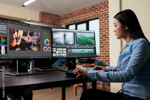 Asian professional video editor sitting at multi monitor workspace while enhancing movie footage quality using advanced software. Post production house team leader editing film frames. photo