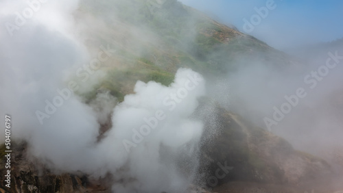 The hillside is shrouded in thick dense steam from an erupting geyser. Poor visibility. The blue sky is visible through the haze. Kamchatka. Valley of Geysers