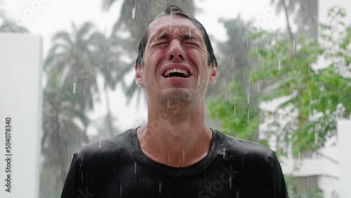 Portrait of crying sad man standing in the pouring rain and getting soaked. Slow motion shot
