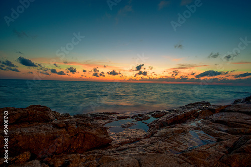 Blurred nature background of the morning sun by the sea, a beautiful golden light, among the trees, rocks and local fishing boats, the beauty of nature during the day.