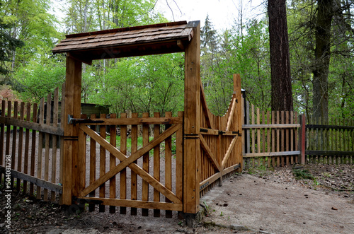 wooden fencing game fields. plank gate with a roof over the gate. dirt road with wooden drainage gutters. small gate with a roofed roof and vertical fencing