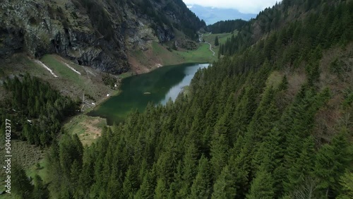 Aerial establish beautiful small green lake in the Swiss alps, drone over forest