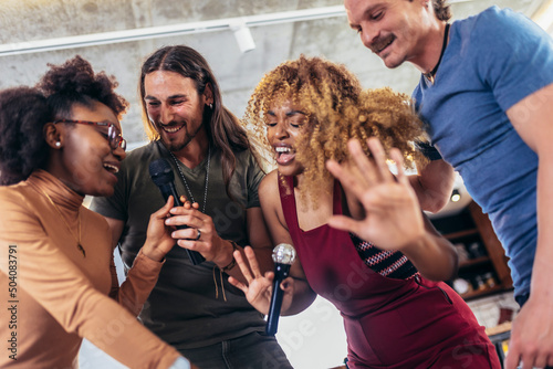 Group of young multicultural friends having party singing song using microphone at home.