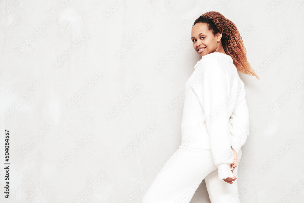 Beautiful black woman with afro curls hairstyle. Smiling model dressed in white summer costume. Sexy carefree female posing near grey wall in studio. Tanned and cheerful. Isolated Beautiful black woman with afro curls hairstyle. Smiling model dressed in white summer costume. Sexy carefree female posing near grey wall in studio. Tanned and cheerful. Isolated