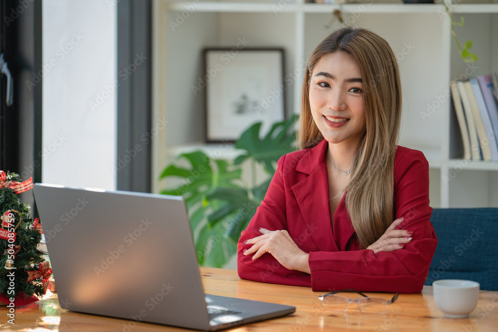 Portrait of young businesswoman using laptop, smiling and looking at camera while sitting at office desk in modern office. Portrait of young businesswoman using laptop, smiling and looking at camera while sitting at office desk in modern office.