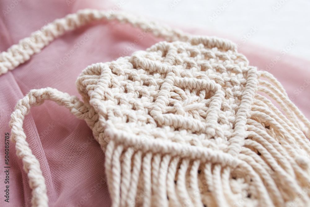 Handmade macrame bag  on pink background. ECO friendly natural macrame cotton bag for woman. Hobby knitting handmade macrame. Modern summer concept.