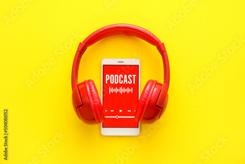 Mobile phone with word PODCAST on screen and headphones on yellow background
