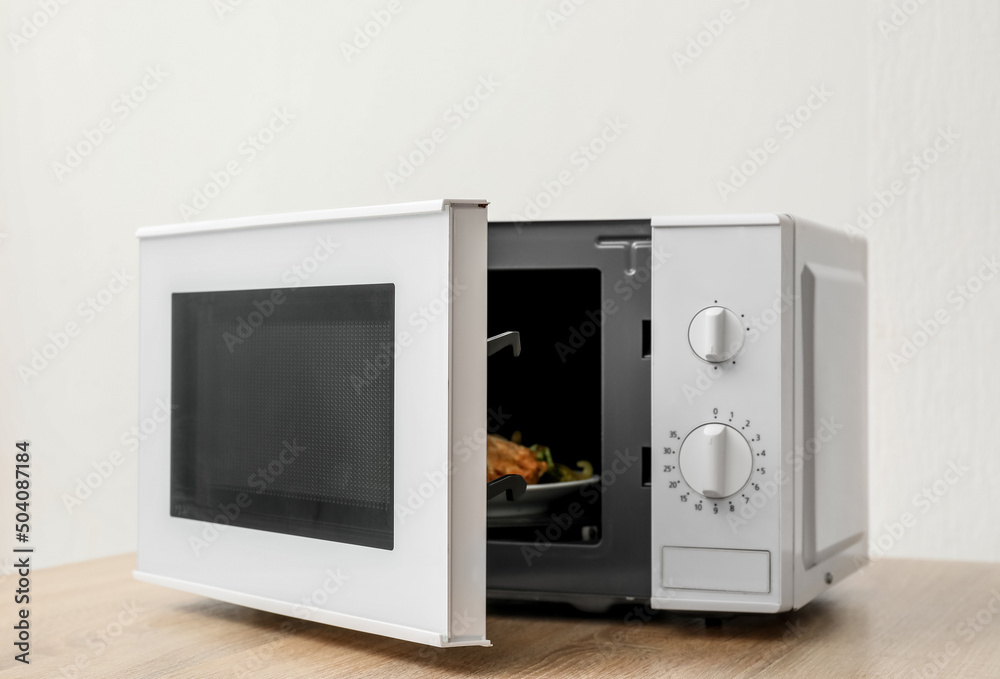 Fototapeta premium Microwave with opened door on wooden table against light background