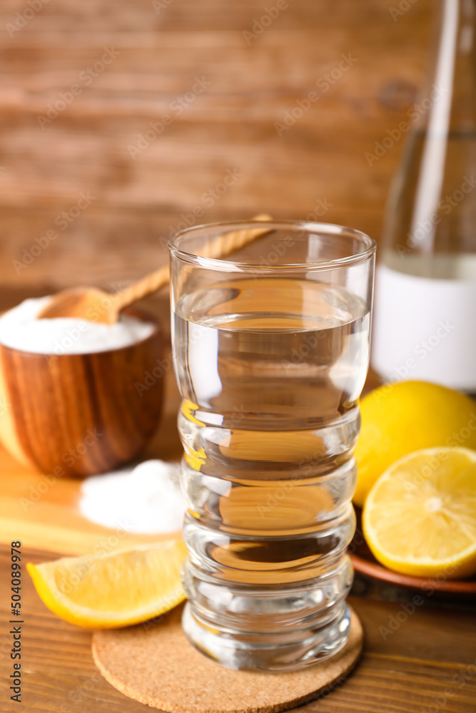 Glass of water, ripe lemons and baking soda on wooden background, closeup
