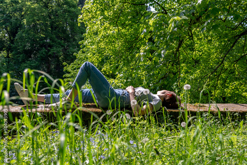 Woman with brown hair, gray t-shirt and jeans lying down on a stone wall in the nature, relaxing and taking a sunbath