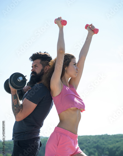 Sporty woman in sexy pink sportswear. Sportive fitness couple, bearded man and sexy woman working out outdoors, sportive couple training with dumbbells, muscular coupl outdoor.