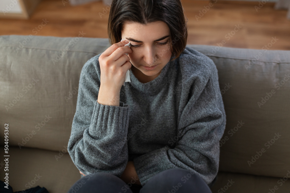 mental health, psychological problem and depression concept - sad crying woman with paper tissue sitting on sofa at home