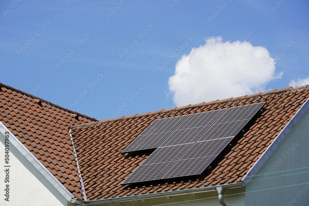 Ziegeldach auf dem Solar Panele installiert sind. Die einzelen runde Wolke lockert den strahlend blauen Himmel etwas auf Ziegeldach auf dem Solar Panele installiert sind. Die einzelen runde Wolke lockert den strahlend blauen Himmel etwas auf