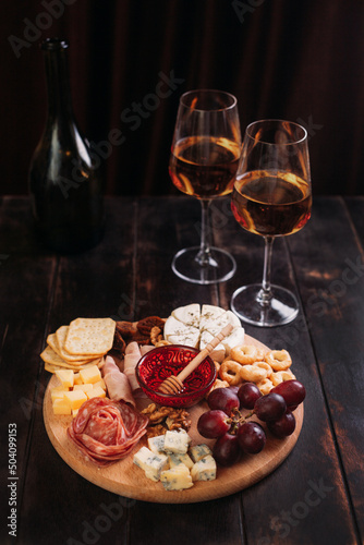 Sausage and cheese cut on round board with fruit, cookies and sauce with two glasses of white port and a bottle