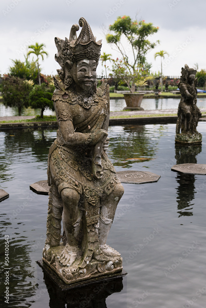 Exquisite ancient monument on indonesian culture, history and balinese religion - stony statue of human warrior deity or demon in beautiful Tirta Gangga park on Bali, vertical. Amazing travel on Bali.