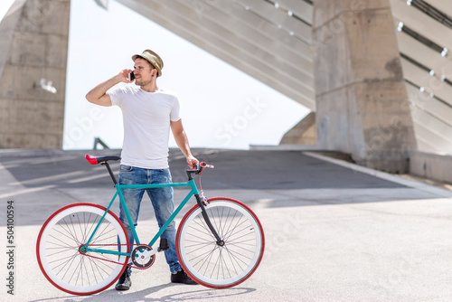 Outdoor portrait of handsome young man with mobile phone and fixed gear bicycle in the street.