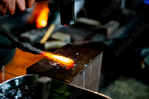 Japanese blacksmith is hammering the hot red steel to make a small Japanese sword. 