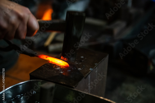 Japanese blacksmith is hammering the hot red steel to make a small Japanese sword. 