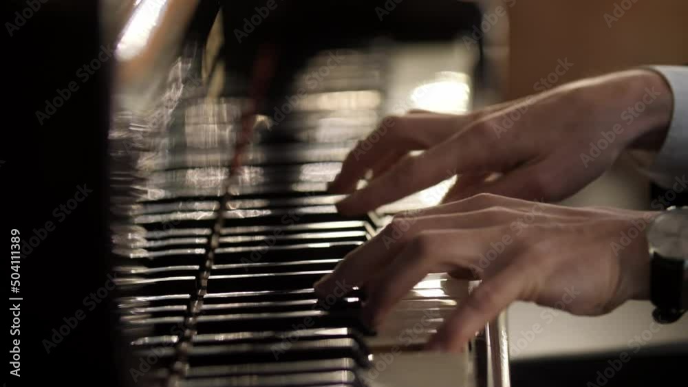 Male hands playing grand piano. Man touches fingers on keys. Professional pianist plays two hands classical music on a beautiful grand piano on stage in concert. Close up. 