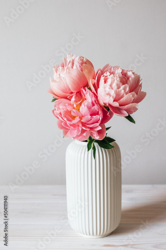 Beautiful bunch of fresh Coral Charm peonies in full bloom in vase against white background. Minimalist floral still life with blooming flowers. © Iryna