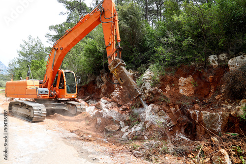 Excavator crusher machine breaks rocks to widen road