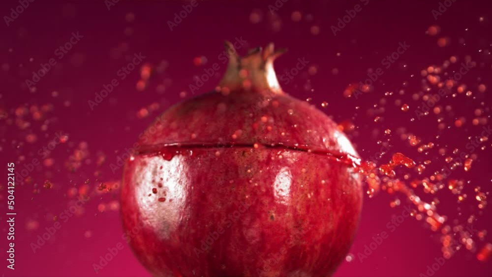 Half Pomegranate falling and splashing on fuchsia background. Food levitation concept. Slow Motion