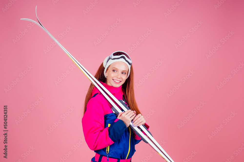 Portrait of sexy smiling redhaired ginger woman in warm clothes professional skier in studio pink background.knitted headband ,warm overalls Portrait of sexy smiling redhaired ginger woman in warm clothes professional skier in studio pink background.knitted headband ,warm overalls
