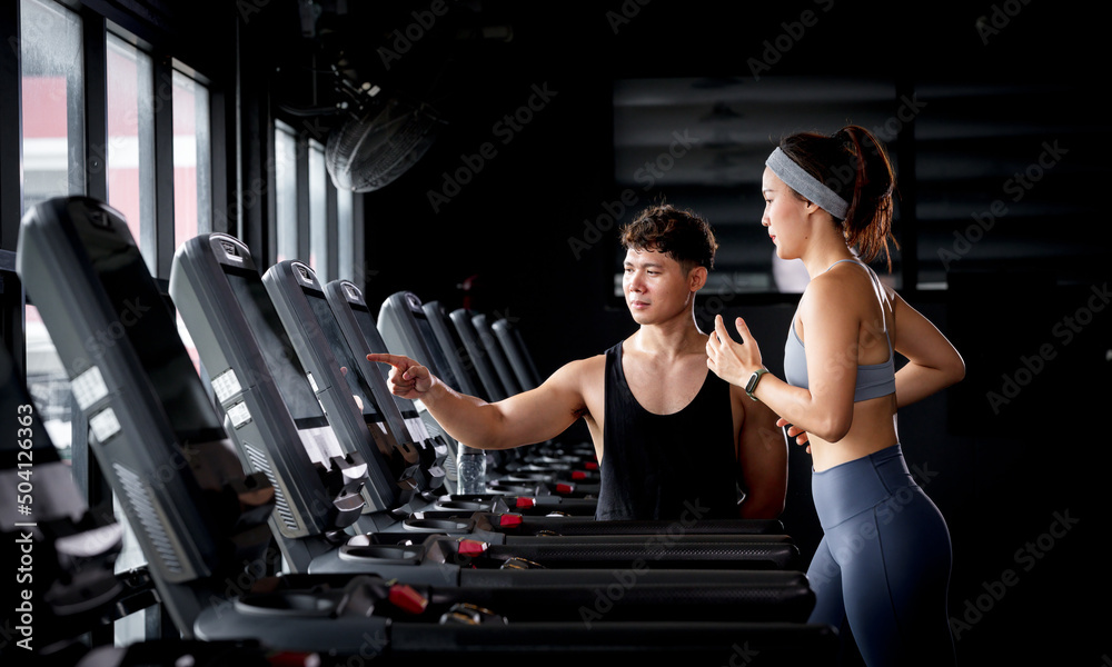 Individual training with a trainer on a treadmill. The trainer controls correctness of the exercise when using a treadmill for cardio, trainer assisting with treadmill screen options at gym. Individual training with a trainer on a treadmill. The trainer controls correctness of the exercise when using a treadmill for cardio, trainer assisting with treadmill screen options at gym.