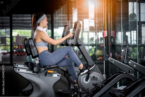 Fitness woman wearing sportwear and workout headband on in the gym. Woman is setting setup machine stationary bike screen options at gym.