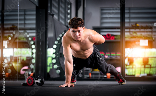Determined athletic guy in sportswear exercise doing push ups by one hand as part of CrossFit bodybuilding training at gym is Muscular body building in fitness lifestyle. © APchanel
