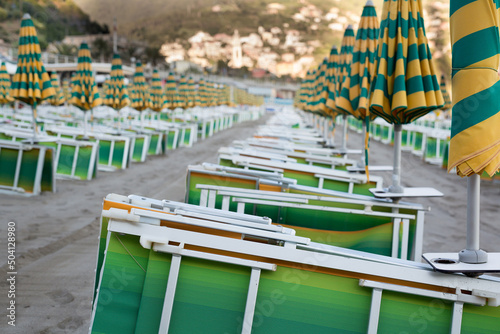 Many closed sun umbrellas and deckchairs on the sandy beach of the resort in summer photo