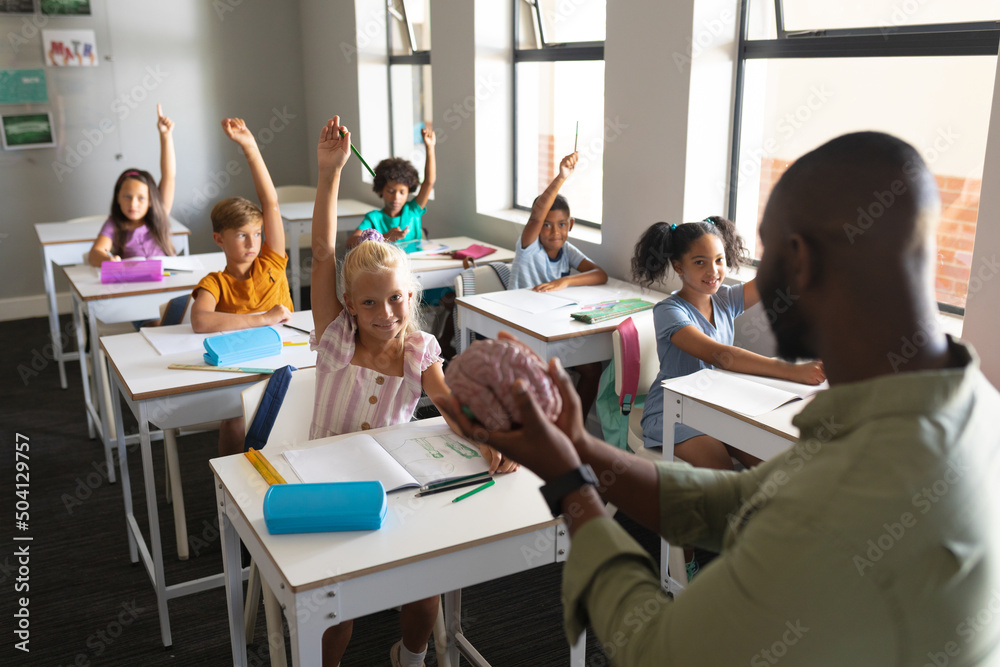 African american young male teacher showing brain model to multiracial students with hand raised