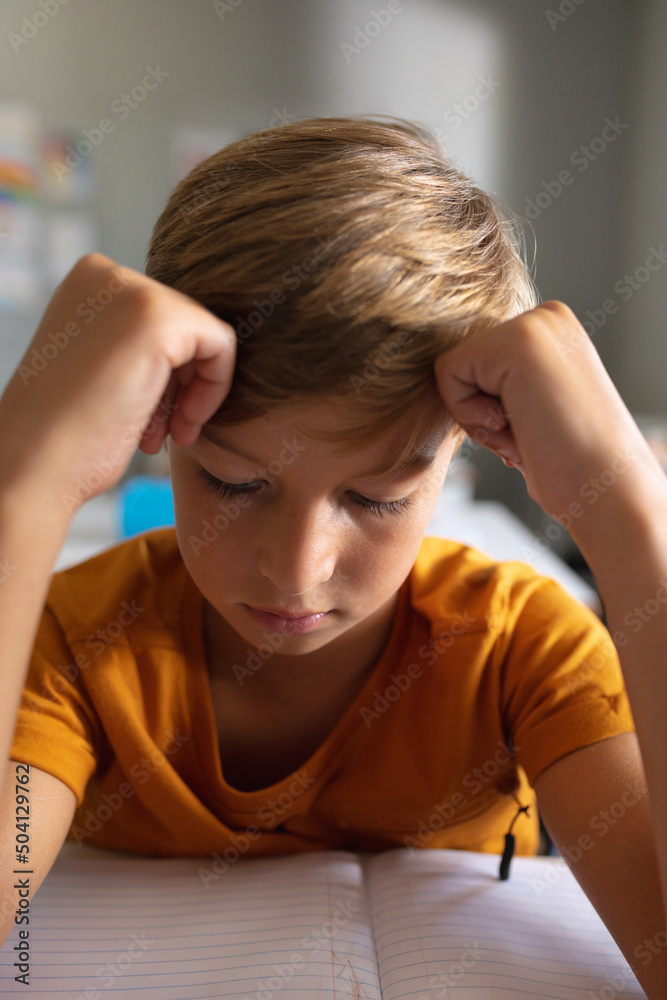 Close-up of caucasian elementary schoolboy with head in hands studying at desk in classroom Close-up of caucasian elementary schoolboy with head in hands studying at desk in classroom