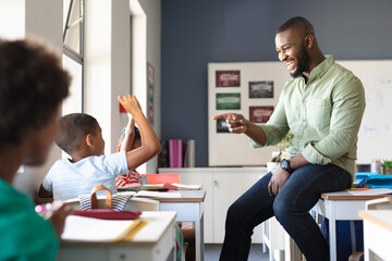 Smiling african american young male teacher gesturing on african american elementary boy at desk