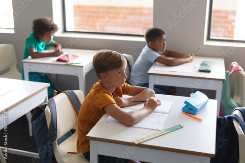 Multiracial elementary students looking away while sitting at desk in classroom