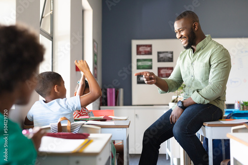 Smiling african american young male teacher gesturing on african american elementary boy at desk