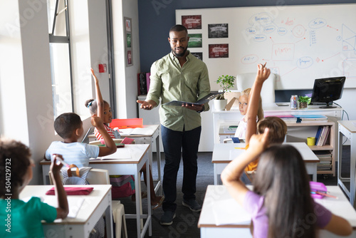 African american young male teacher with file standing by multiracial students with hand raised