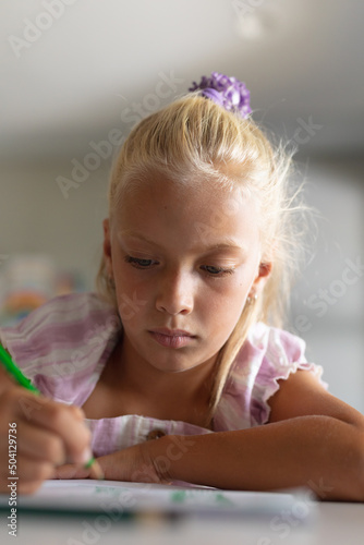 Close-up of caucasian elementary schoolgirl drawing on book at desk in classroom