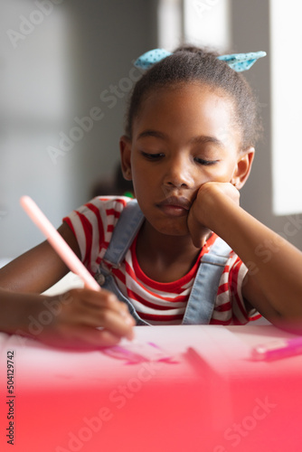 Close-up of african american elementary schoolgirl drawing on book at desk in classroom