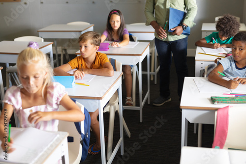 Multiracial elementary students studying at desk with african american young male teacher in class