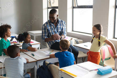 Happy multiracial elementary students looking at multiracial young male teacher showing brain model